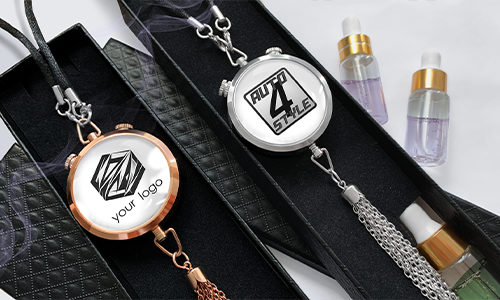 Two round pendants in black boxes: rose gold with geometric logo, silver AUTO 4 STYLE, tassels and chains, bottles behind