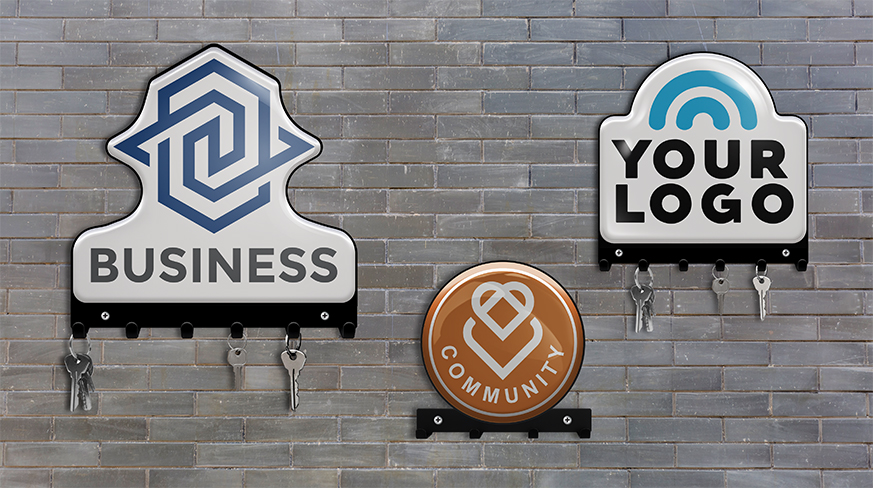 Three wall key holders on brick wall: BUSINESS with blue logo, YOUR LOGO with arc, COMMUNITY with heart, keys hanging
