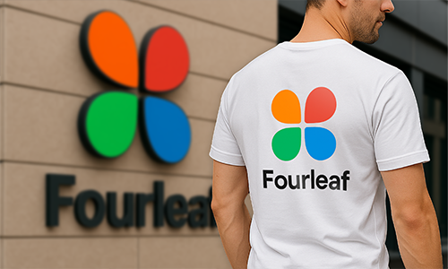Homme portant un t-shirt blanc personnalisé avec le logo coloré “Fourleaf” correspondant à la marque sur le mur du bâtiment en arrière-plan.