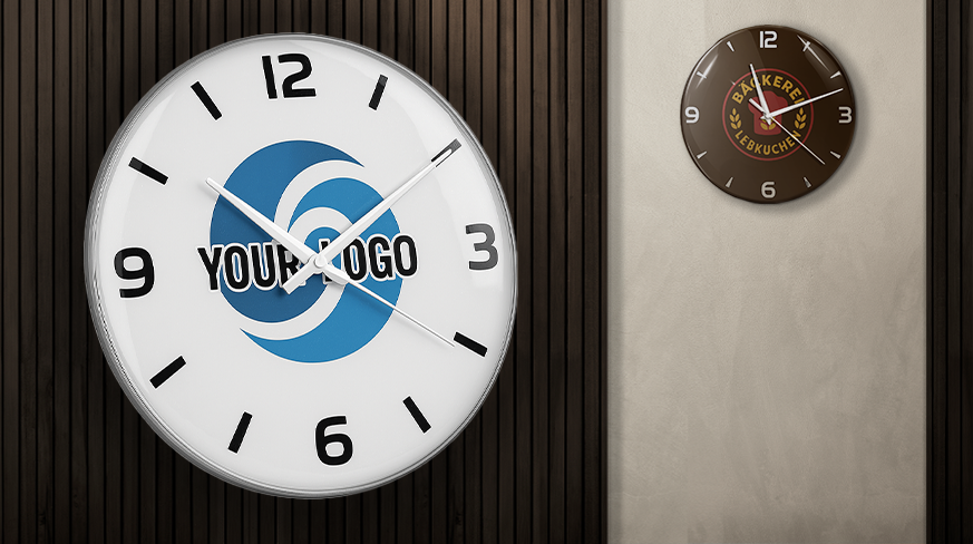 Two wall clocks: left white face YOUR LOGO at 10:10 on dark wood panel, right brown BAKERY SELKUCHEN at 2:50 on light wall