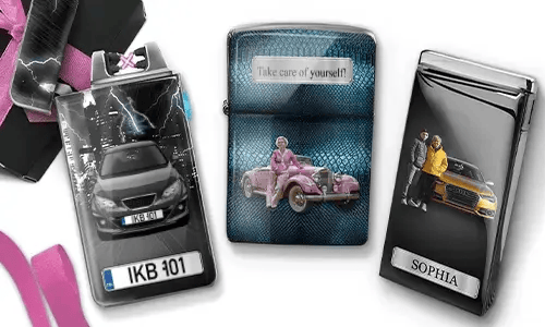 Drei Metallfeuerzeuge mit personalisierten Designs. Das linke Feuerzeug zeigt eine Stadtsilhouette und ein Paar neben einem Auto mit der Aufschrift „BESTE OMA DER WELT“. Das mittlere Feuerzeug stellt ein rosafarbenes Oldtimer-Auto dar, darüber steht „HAB DICH LIEB OMA“. Das rechte Feuerzeug zeigt ein blaues Auto und ein Kennzeichen. Rosafarbene Schleifen verleihen dem Ganzen einen Geschenkcharakter.