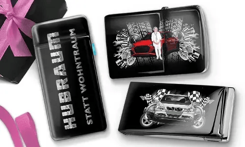 Drei Zigarettenetuis in Schwarz und Silber mit dynamischen Auto-Grafiken. Eines trägt die Aufschrift „Hubraum statt Wohntraum“, während die anderen Rennmotive zeigen.