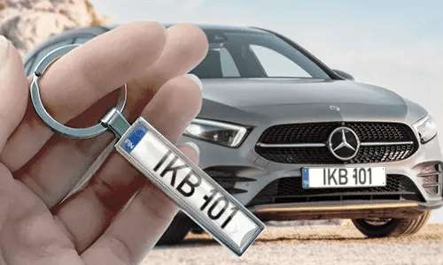 Tegneserie-nummerskilt-nøkkelring holdt i hånden med matchende bilskilt i bakgrunnen